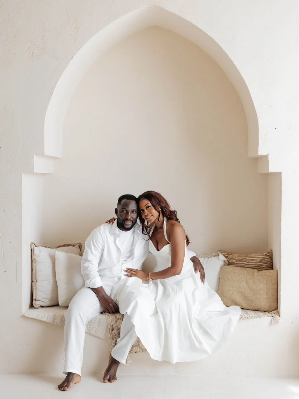 Otobong and Harrison in white, seated beneath the cream architectural arch